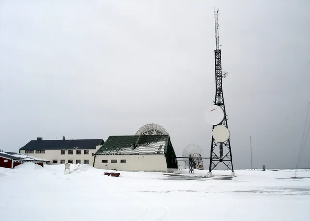 The white buildings of Isfjord Radio in the snow, with a tall lattice radio mast and satellite dishes beside them